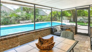 Un patio cubierto con piscina, mobiliario exterior y vistas al jardín trasero.