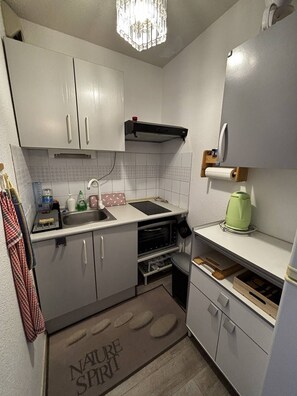 Une cuisine compacte avec des meubles blancs, un four encastré, un évier et un petit plan de travail.
