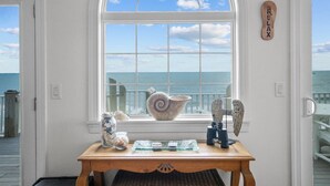 Een kamer met een groot rondboogvenster met uitzicht op de zee, een houten tafel met decoratieve objecten en een bordje met de tekst 'RELAX'.