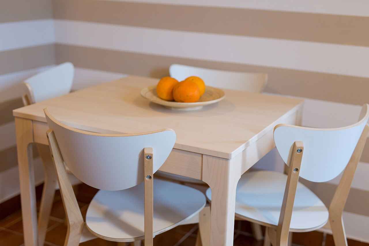 Una mesa de comedor con un plato de naranjas, rodeada de sillas blancas.