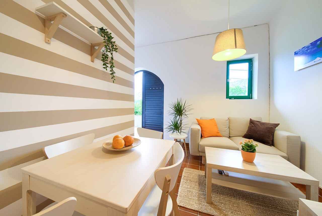 Uma sala de estar moderna com um sofá, uma mesa de jantar com cadeiras e uma planta pendente.