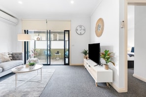 Ein modernes Wohnzimmer mit Sofa, Couchtisch, Fernseher und Pflanzen.