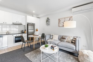 A modern kitchen with white cabinets, a built-in oven, and a dining area with a table and chairs.