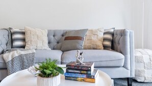 Un salon moderne avec un canapé gris, des coussins à rayures et une pile de livres sur une petite table d’appoint blanche.