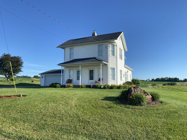 A two-story white house with a porch, surrounded by a well-maintained lawn and a large tree. - Family owned and operated spacious Farm House with a modern decorative flair. (Glenmont)