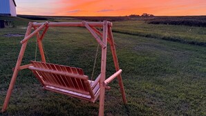 Un columpio de madera en un campo cubierto de césped, con un atardecer de fondo.