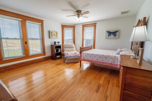 A bedroom with a bed, a chair, a desk, and a ceiling fan. There are windows with blinds and a butterfly painting on the wall. - Family owned and operated spacious Farm House with a modern decorative flair. (Glenmont)