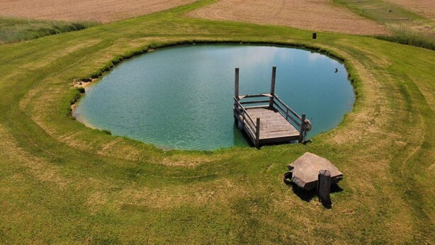 Un estanque circular con un muelle de madera y una estructura de piedra.
