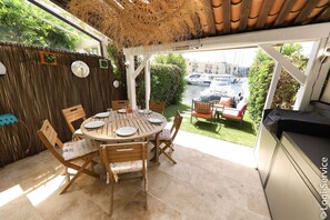 A covered patio with a round wooden table set for dining, surrounded by wooden chairs.