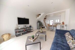 A spacious living area with a large TV, a sofa, and a coffee table. There is a staircase leading to an upper level.