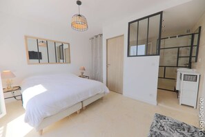 A bedroom with a bed, a bedside table with a lamp, a hanging light fixture, a large mirror, and a wardrobe.