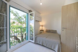 A bedroom with a bed, a window with a view of greenery, and an air conditioning unit.