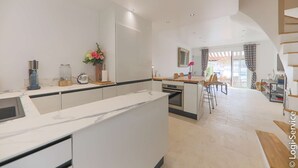 Eine moderne Küche mit weißen Schränken, einer Marmorarbeitsplatte und einem Essbereich mit Holztisch und Stühlen.