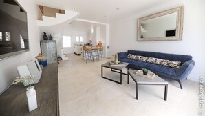 Ein geräumiges Wohnzimmer mit einem blauen Sofa, einem Couchtisch und einer Essecke im Hintergrund.