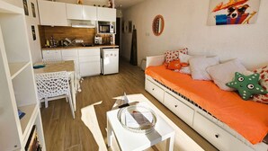 Un espace de vie compact comprenant un coin cuisine, un coin repas et un canapé agrémenté d’une literie orange.