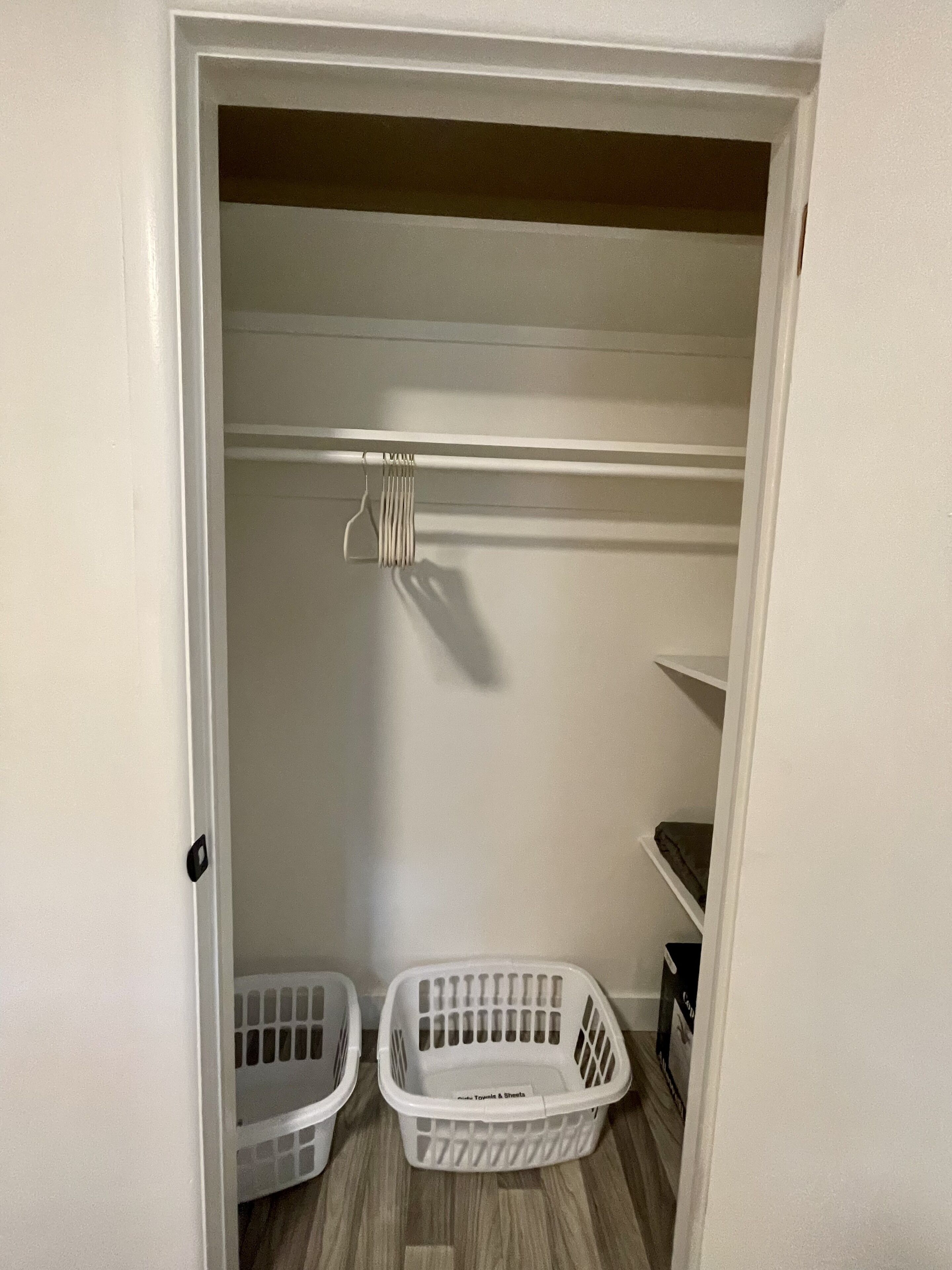 Un armario con espacio para colgar y estantes, que contiene dos cestos blancos para ropa.
