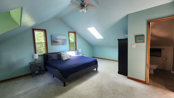 A bedroom with a bed, two bedside tables, a ceiling fan, and a skylight.