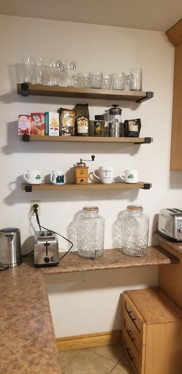 Une cuisine avec des étagères où sont rangés de la verrerie, des produits liés au café et un moulin à café.