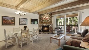 Una sala de estar acogedora con chimenea de piedra, vigas de madera en el techo y un balcón con mobiliario exterior.