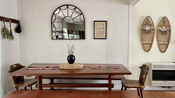 A dining area with a wooden table, benches, a vase with dried flowers, a mirror, and wall-mounted baskets.