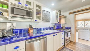 Una cocina moderna con armarios blancos, encimeras de azulejos azules y electrodomésticos de acero inoxidable, incluyendo un horno empotrado.