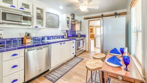 Una cocina moderna con armarios blancos, encimeras con azulejos azules, electrodomésticos de acero inoxidable y una mesa de comedor de madera con servilletas y vasos azules.