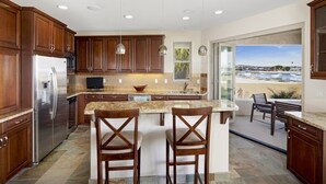 A modern kitchen with wooden cabinets, a stainless steel refrigerator, granite countertops, and a large island with two bar stools. - 3526 -Bayside Walk Unit  2 (San Diego)