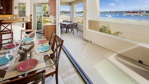 A dining area with a table set for four, a kitchen with dark wooden cabinets, and a view of the beach with boats. - 3526 -Bayside Walk Unit  2 (San Diego)