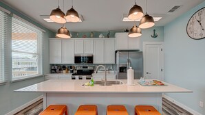 A modern kitchen with white cabinets, a large island with stools, and pendant lighting.
