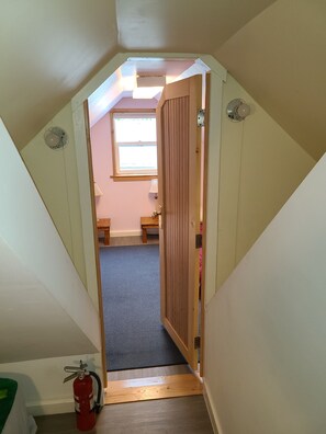 Kapeat portaat johtavat huoneeseen, jossa on ikkuna, puuovi ja lattialla palosammutin.