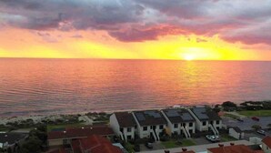 A coastal view with a sunset over the ocean, residential buildings with solar panels, and a clear sky. - Luxurious beachfront, panoramic views (West Lakes Shore)
