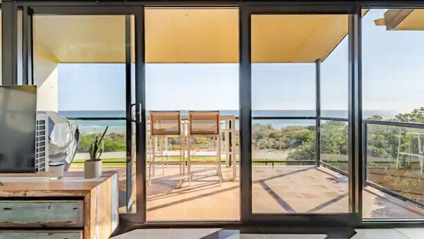 A modern room with a sliding glass door leading to a balcony with a view of the sea. - Luxurious beachfront, panoramic views (West Lakes Shore)