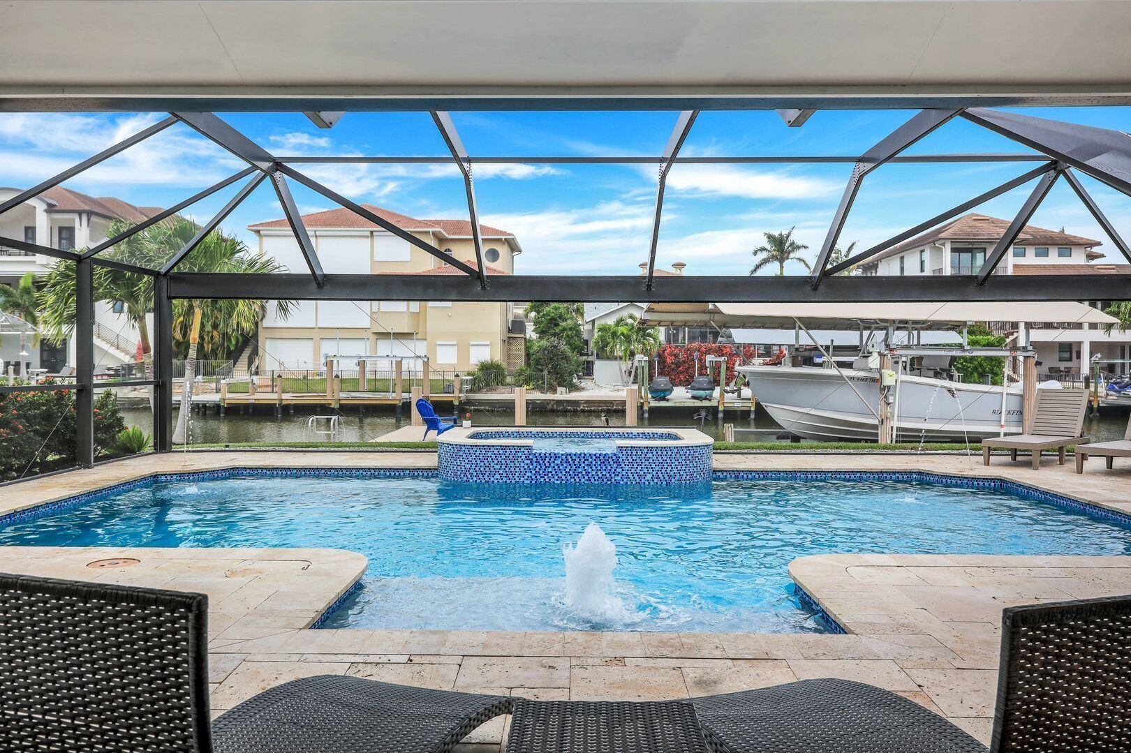 A covered swimming pool with a hot tub, lounge chairs, and a view of boats and houses.