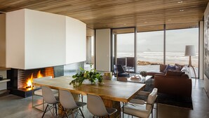 A modern interior with a large wooden dining table, comfortable seating, a fireplace, and a view of the ocean. - Luxury Designer Beachfront Home 3 Bed, 3.5 Bath in Arch Cape, Oregon. (Arch Cape)
