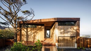 A modern house with a wooden exterior, a front door, and a pathway leading to the entrance. - Luxury Designer Beachfront Home 3 Bed, 3.5 Bath in Arch Cape, Oregon. (Arch Cape)