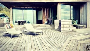 A modern outdoor deck with lounge chairs and a wooden pergola. - Luxury Designer Beachfront Home 3 Bed, 3.5 Bath in Arch Cape, Oregon. (Arch Cape)