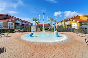 A courtyard with a central water feature, surrounded by multi-story buildings with balconies and a brick floor.