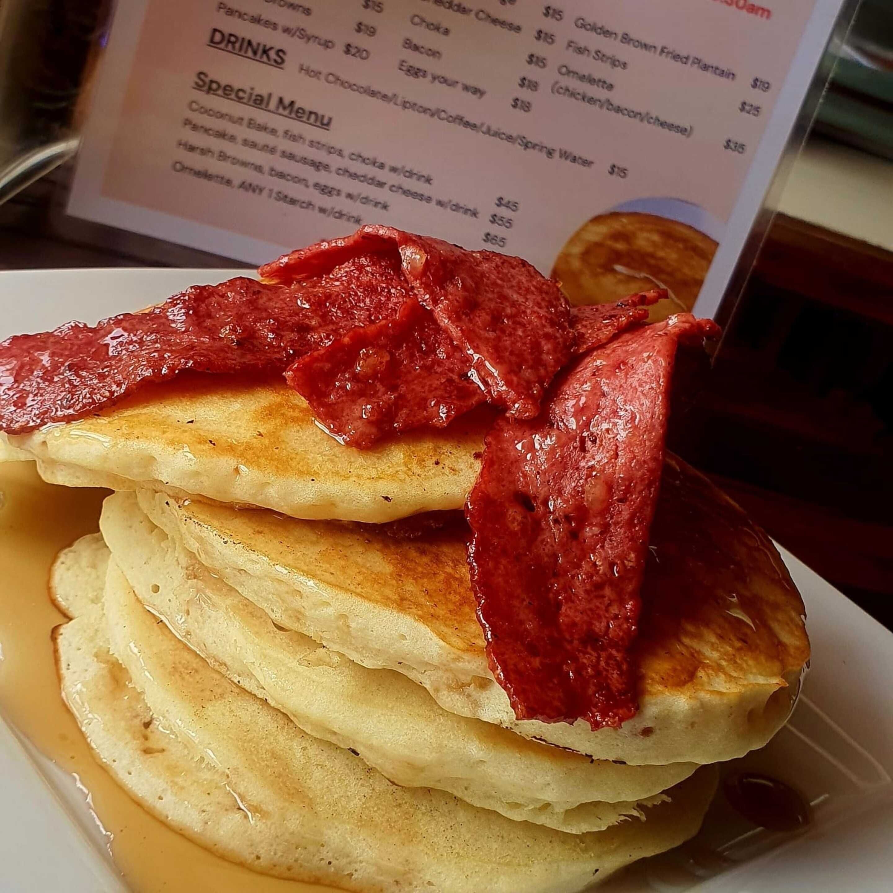 A stack of pancakes topped with red syrup and a menu in the background.
