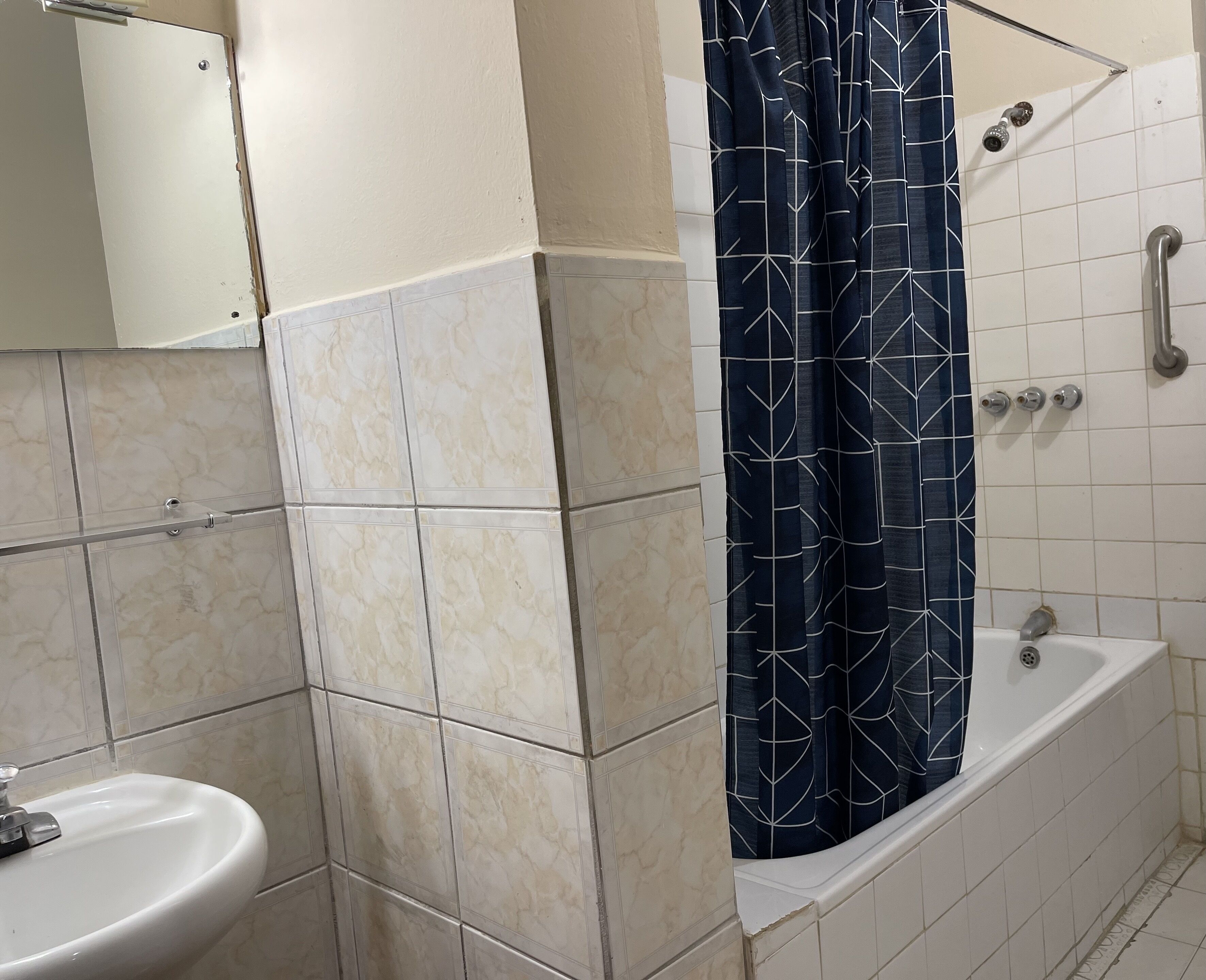 A bathroom with a sink, a shower with a blue patterned curtain, and a toilet.