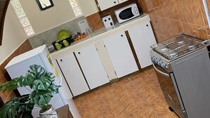 A kitchen with white cabinets, a microwave, and a gas stove. - St Ann's Guest House Ltd. (Port of Spain)