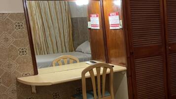 Una habitación pequeña con un armario de madera, una cama con cortina a rayas, una mesa de madera con una silla y un televisor montado en la pared.