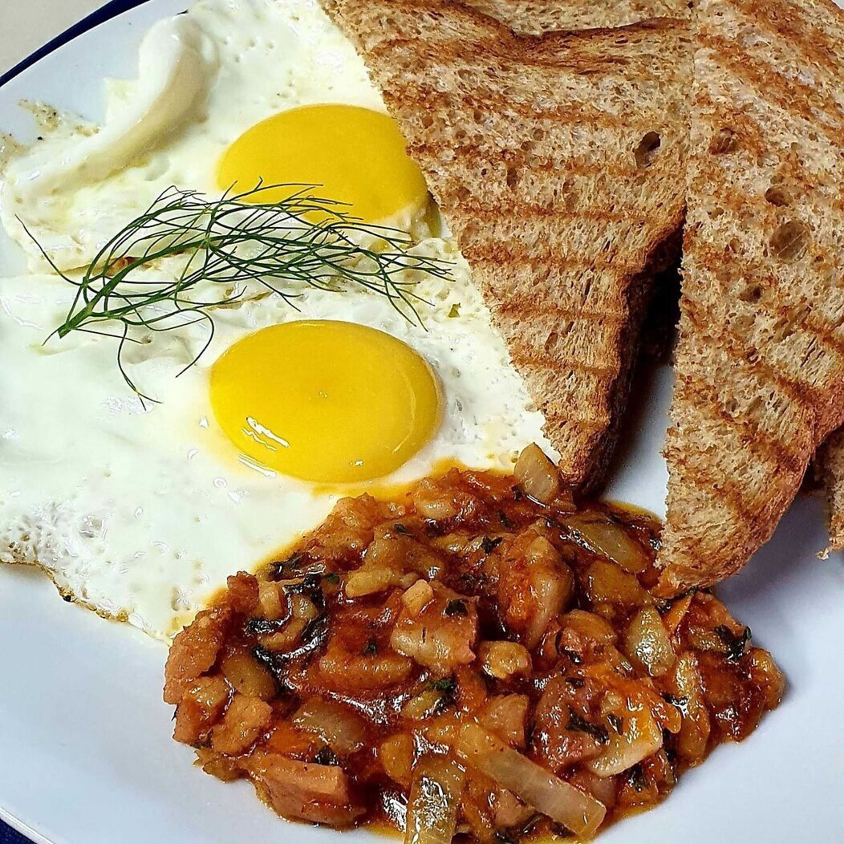 A plate with two fried eggs, a slice of toast, and a serving of sautéed onions.