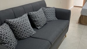 A grey sofa with patterned cushions in a room with tiled flooring. - St Ann's Guest House Ltd. (Port of Spain)