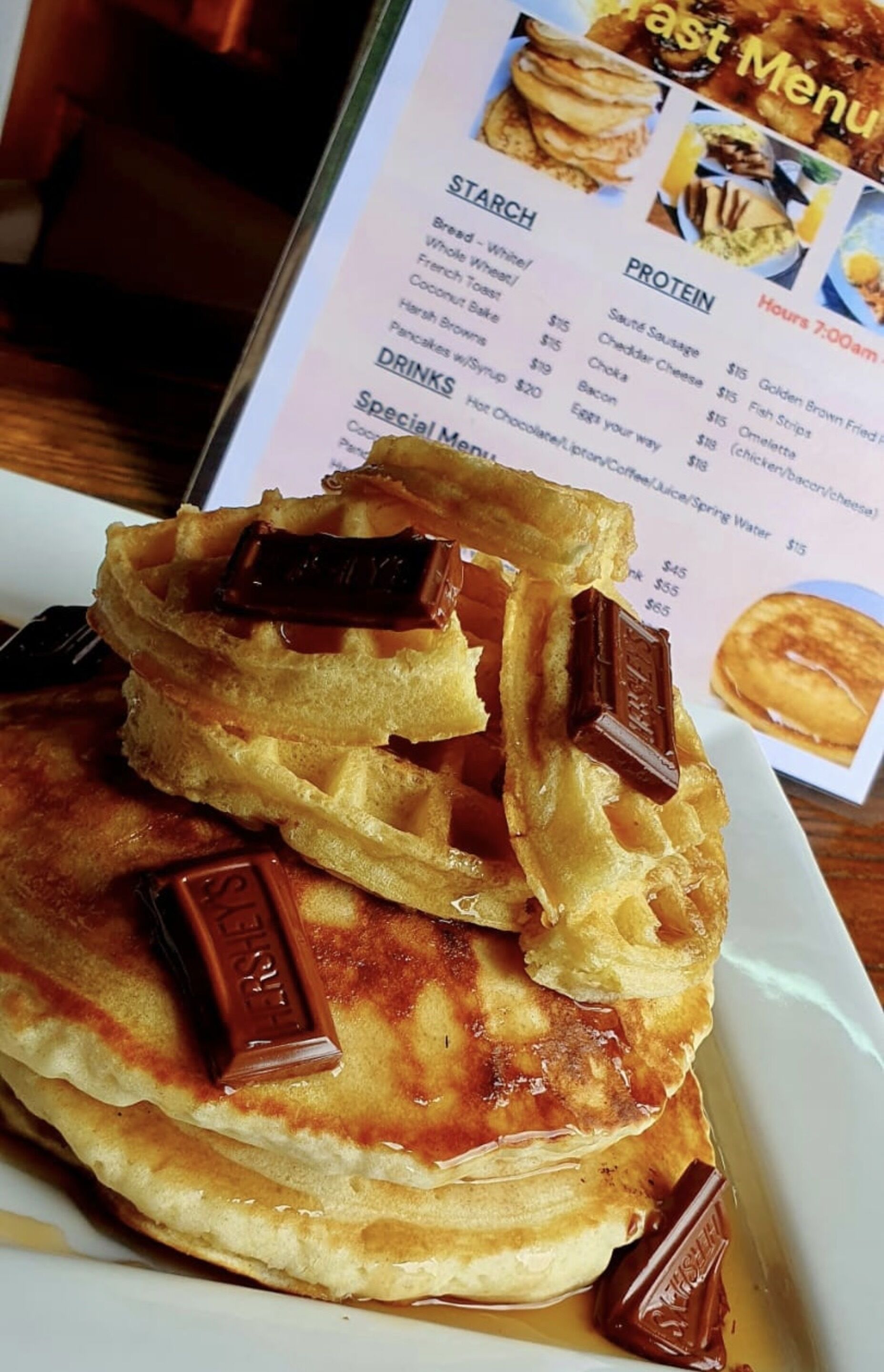 A stack of waffles with chocolate pieces on a white plate, with a menu in the background.
