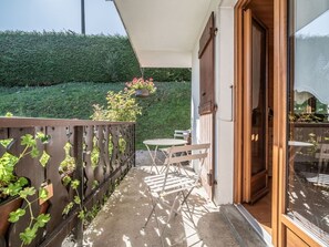 Enjoy a serene retreat with a wooden deck, table, and chairs, surrounded by a lush hedge and grassy lawn.