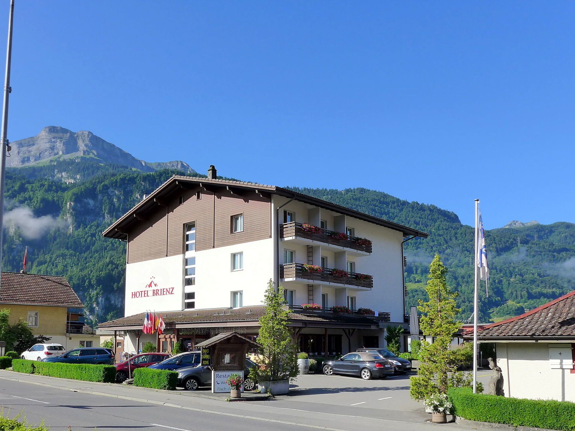 Ein zweistöckiges Hotel mit Balkonen, einem Schild mit der Aufschrift "HOTEL BRIENZ" und einer Bergkulisse im Hintergrund.