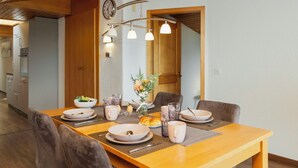 A dining area with a wooden table set for four, surrounded by chairs, and a modern light fixture above.