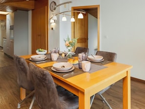 Zona pranzo con tavolo in legno apparecchiato per quattro persone, circondato da sedie e un lampadario moderno.