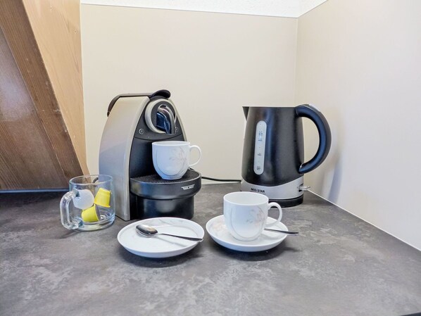 A coffee maker, a kettle, two cups, and a glass with a spoon on a countertop.