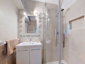 Ein modernes Badezimmer mit Duschkabine aus Glas, einem weißen Waschbecken mit Spiegel darüber und einem Handtuchhalter.